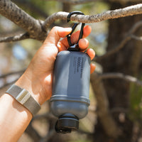 Image of nestout 10k grey colored cylinder battery pack hanging upside down from hook on tree branch | features military IP67 rating | stores up to 10000N of power | rugged waterproof design | compact size | versatile charging | to be used with NESTOUT solar panels, fans, lamps, and flashes