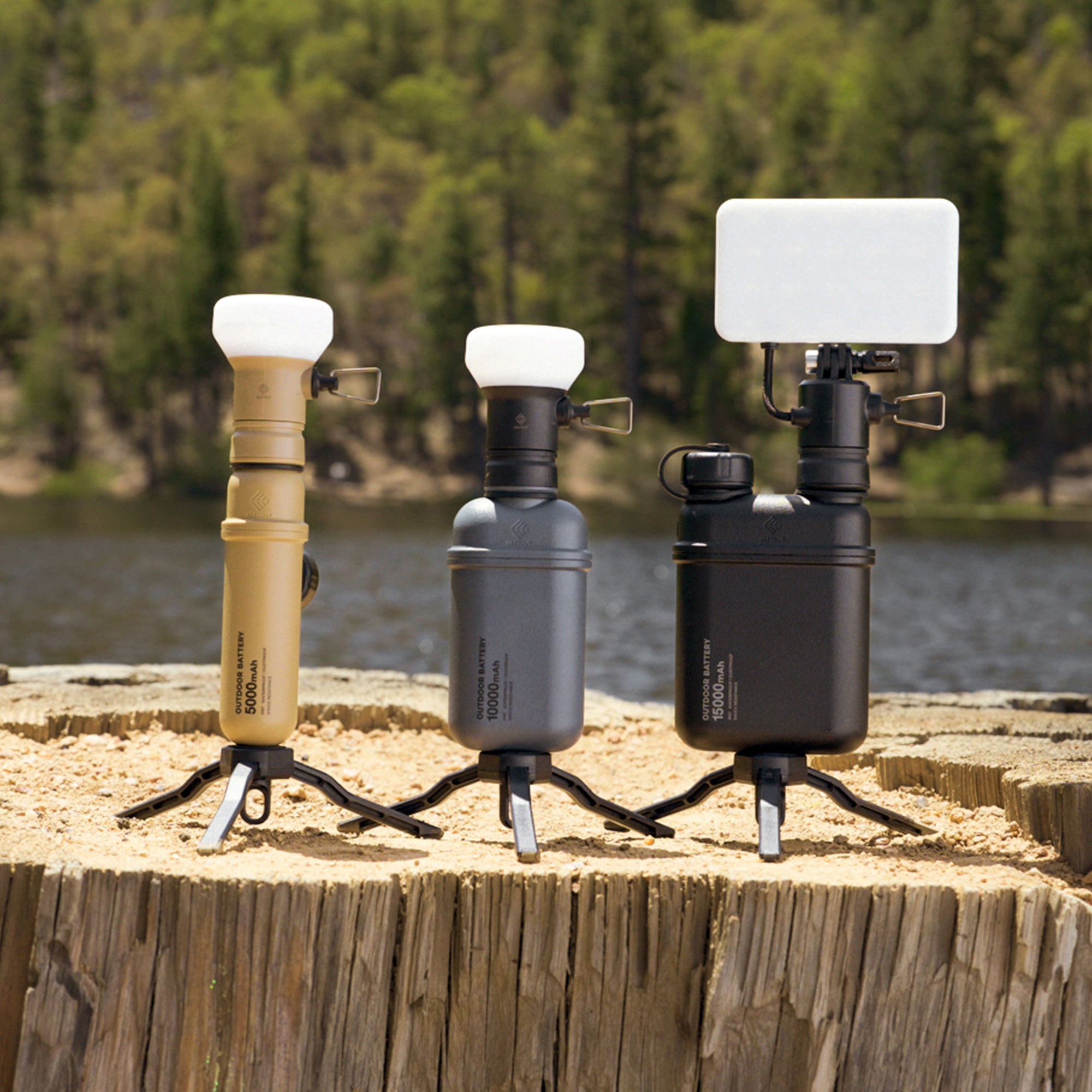 Image of nestout 15k black 5k beige 10k grey colored cylinder battery packs on a tree stump | features IP67 rating | stores up to 15000N of power | rugged waterproof design | compact size | versatile charging | to be used with NESTOUT solar panels, fans, lamps, and flashes