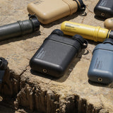 Image of nestout 15k black 5k olive 10k grey 5k mustard 15k beige colored cylinder battery packs laying on tree stump | features military IP67 rating | stores up to 15000N of power | rugged waterproof design | compact size | versatile charging | to be used with NESTOUT solar panels, fans, lamps, and flashes
