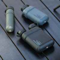 Image of nestout 15k black 10k grey 5k olive colored cylinder battery packs laying on a table | features military IP67 rating | stores up to 15000N of power | rugged waterproof design | compact size | versatile charging | to be used with NESTOUT solar panels, fans, lamps, and flashes