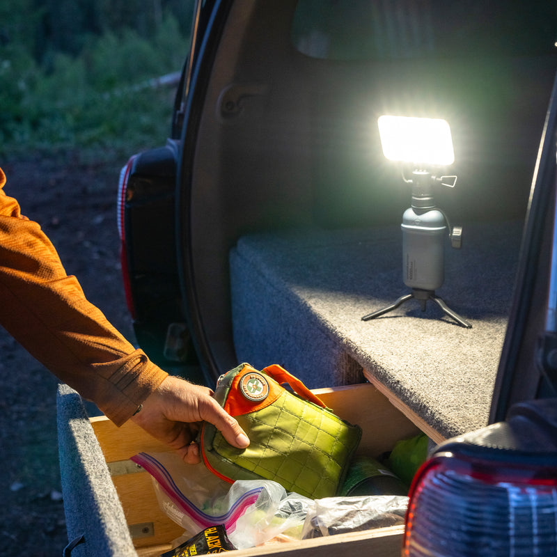Image of nestout 15k grey colored cylinder battery pack connected to flash being used trunk of SUV | features military IP67 rating | stores up to 15000N of power | rugged waterproof design | compact size | versatile charging | to be used with NESTOUT solar panels, fans, lamps, and flashes