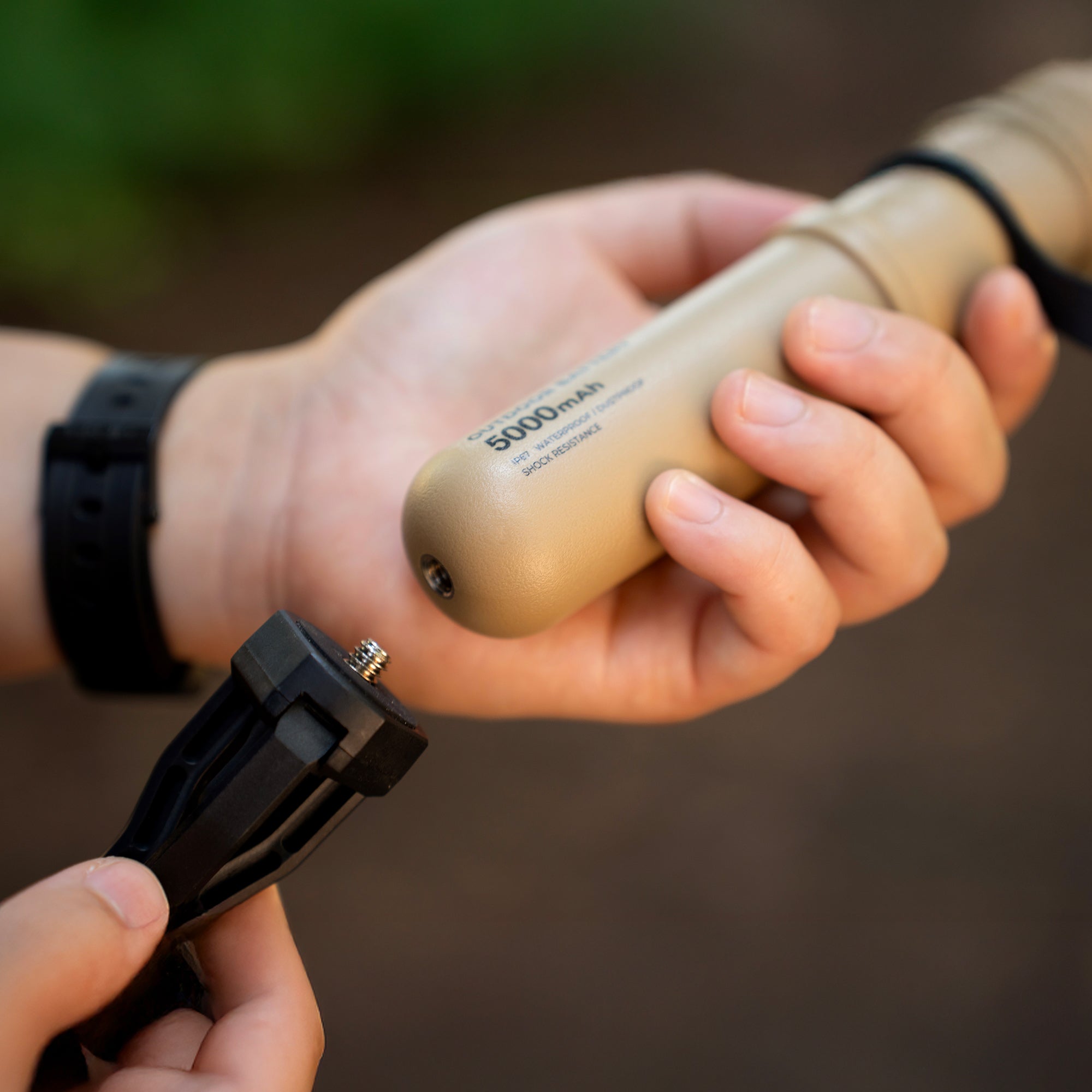 image of hand screwing tripod to bottom of nestout beige colored cylinder battery pack | features military IP67 rating | stores up to 5000N of power | rugged waterproof design | compact size | versatile charging | to be used with NESTOUT solar panels, fans, lamps, and flashes