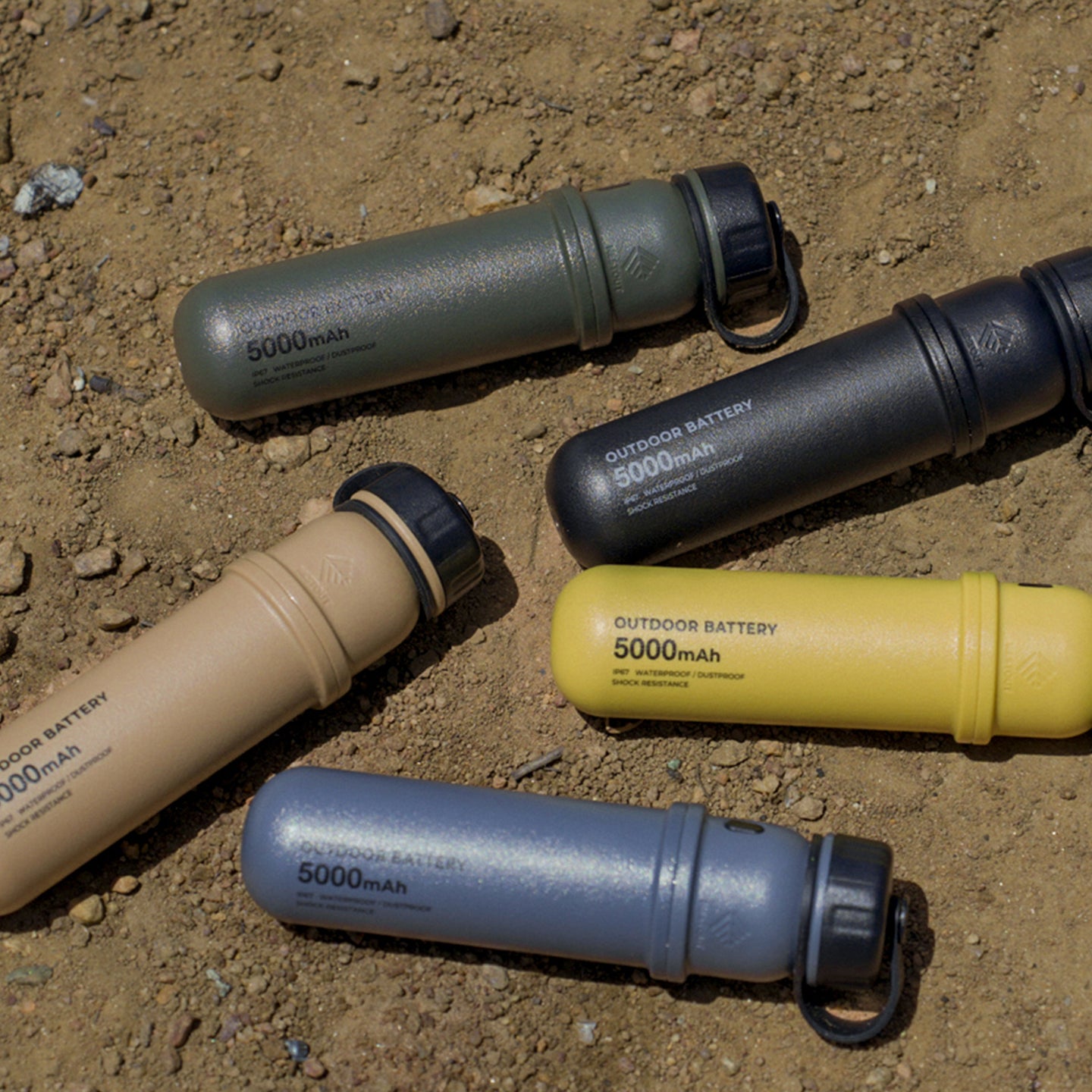 Image of 5k nestout olive colored cylinder battery pack next to black beige mustard and grey colored batteries | feature military IP67 rating | stores up to 5000N of power | rugged waterproof design | compact size | versatile charging | to be used with NESTOUT solar panels, fans, lamps, and flashes