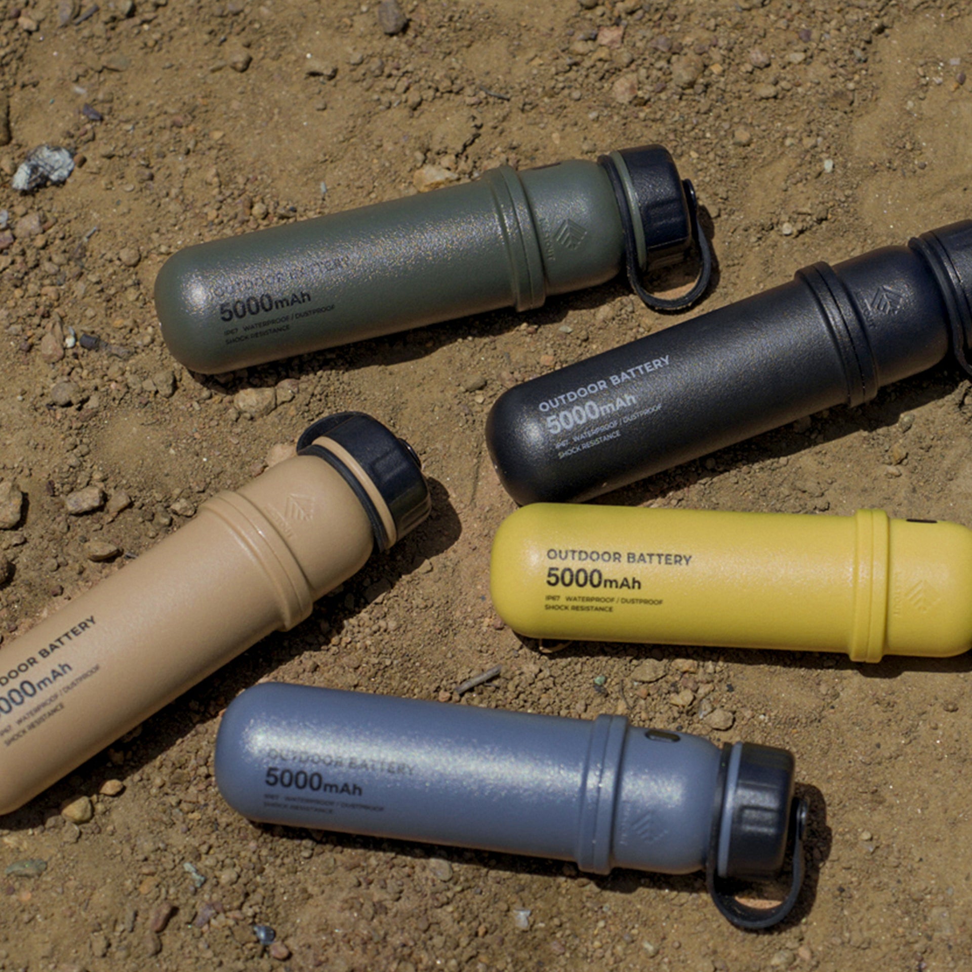 Image of 5k nestout olive colored cylinder battery pack next to black beige mustard and grey colored batteries | feature military IP67 rating | stores up to 5000N of power | rugged waterproof design | compact size | versatile charging | to be used with NESTOUT solar panels, fans, lamps, and flashes